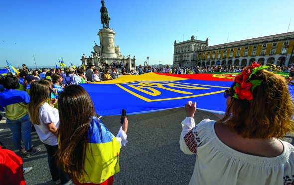 Люди розгортають жовто-блакитний прапор у столиці Португалії Лісабоні на акції підтримки українських біженців 30 квітня