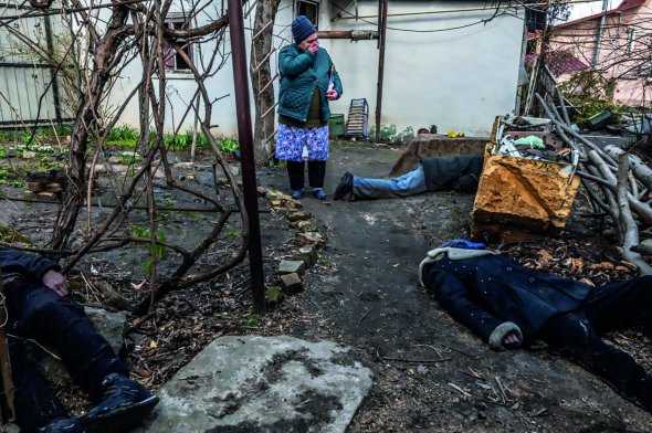 Жителька Бучі оглядає садок, у якому російські військові вбили трьох чоловіків, початок квітня 2022-го. Утримували містечко в окупації протягом березня. Влаштували катівню в підвалі дитячого санаторію, де допитували і стріляли людям у голови. Ґвалтували жінок. Убили понад 320 мирних жителів. Частину поховали у братській могилі біля церкви та по дворах, решта лежала на вулицях і подвір’ях до звільнення населеного пункту Збройними силами України 31 березня