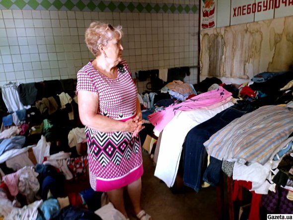 Харків'янка Жанна Костянтинівна допомагає перебирати одяг для переселенців у колишньому хлібному магазині, де нині тече дах
