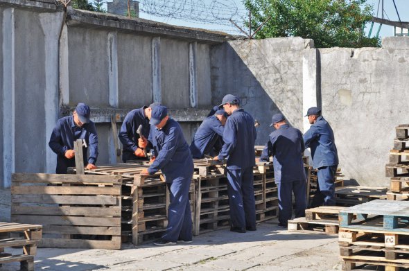 Російські військові виготовляють дерев’яні піддони в таборі для полонених в Україні. Установу створили після початку широкомасштабного вторгнення Росії. Під наглядом охорони полонені можуть вільно пересуватися всередині будівлі. Живуть у багатомісних кімнатах, мають медичне забезпечення, книжки й телевізор. 20 червня 2022 року