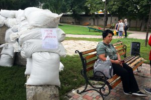 Жінка сидить на лавці в міському парку Чугуєва Харківської області, 26 липня. Поряд розташоване одне з тимчасових укриттів. Його змайстрували з бетонних блоків і мішків із піском. Місцеві ховаються за ним під час артилерійських обстрілів. Російські терористи атакують майже щодня