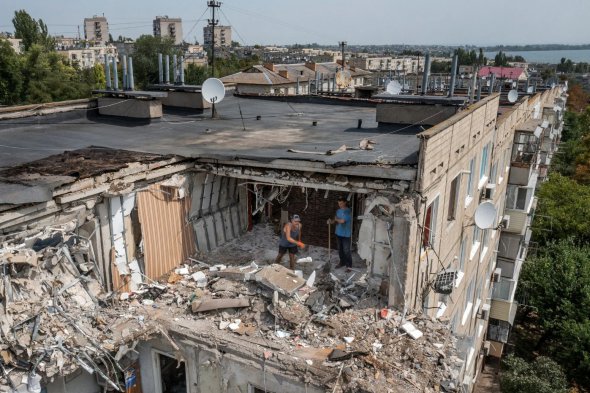 У понеділок українські чоловіки прибирають завали з будинку, недавно ураженого російською ракетою у Нікополі 
