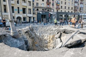 Харківські комунальники стоять навколо величезної воронки від снаряда, 26 серпня. Російські терористи напередодні вночі запустили ракету по центру міста. Влучили в дорогу перед житловим будинком. Від удару повилітали вікна. Одна жінка отримала осколкові поранення