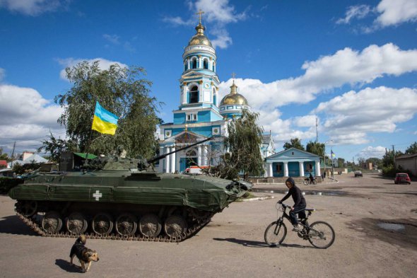 Мальчик едет на велосипеде возле бронированного танка с украинским флагом в Изюме, 19 сентября 