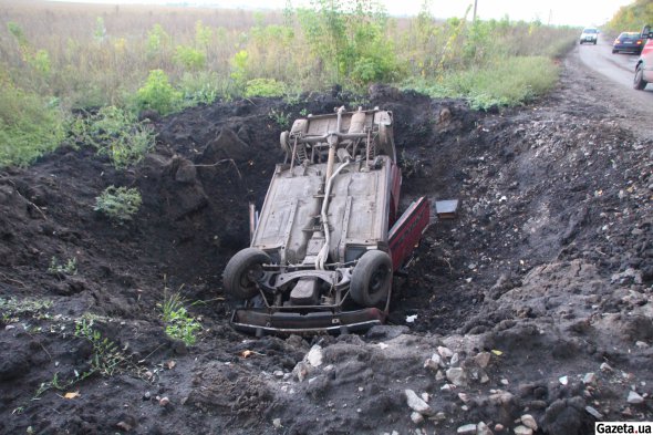 Разбомбленная легковушка лежит в воронке от выбуза на дороге между деревнями