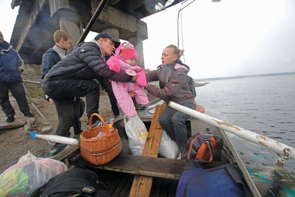 Чоловік переправляє човном сім’ю через Печенізьке водосховище біля села Старий Салтів на Харківщині, 27 вересня 2022 року. Мостом користуватися не можна. Його підірвали українські військові, щоб зупинити просування окупантів на Харків у березні