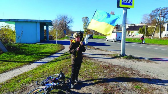 Шестикласник Максим у селі Подвірки махає прапором автомобілям, що їдуть до Харкова. З 24 лютого хлопчик майже щодня приходить на дорогу вітати військових