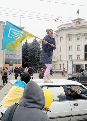 Жінка махає прапором України, стоячи на даху автомобіля в Херсоні 12 листопада. За день до цього місто офіційно оголосили вільним від російських окупантів. Місцеві жителі одразу почали збиратися на центральних вулицях з прапорами. Їх понад вісім місяців ховали від росіян. Переважно закопували в землю