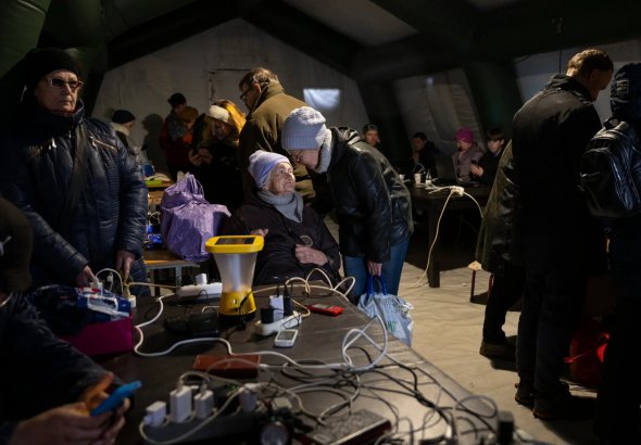 Ксенія Пришва, 93 роки, гріється в наметі в середу в Херсоні. Вона планує евакуюватися через посилення обстрілів, відсутність тепла та електрики 