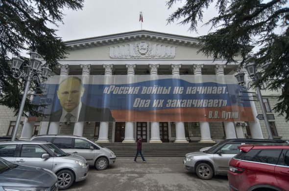 Чоловік йде перед будівлею з великим транспарантом із написом «Росія не починає війни, вона їх закінчує. Володимир Путін» у Ялті, 15 березня 