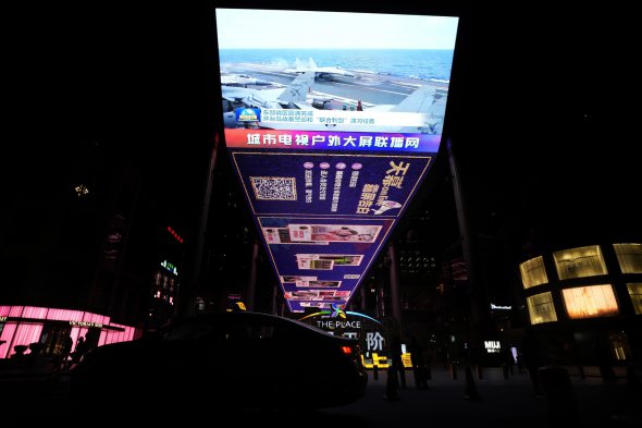 Вечерний выпуск новостей на экране в Пекине показывает китайские истребители на авианосце, 10 апреля.