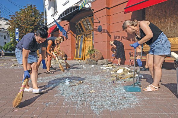 Люди підмітають скло в центрі Чернігова після ракетної атаки росіян 19 серпня. Росіяни цілили в Чернігівський обласний академічний музично-драматичний театр імені Тараса Шевченка. Загинули семеро людей