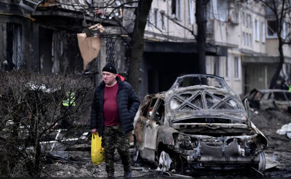 Мужчина ходит возле разбитых авто возле пострадавшего после ракетного удара жилого дома в Киеве, 13 декабря 2023 года 