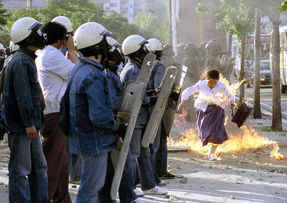 Жительку Сеула зачепило полум’я від пляшки із займистою сумішшю, яку кинули учасники антиурядової демонстрації у столиці Південної Кореї, 25 травня 1988 року. Більшість демонстрантів – студенти, які були незадоволені тим, що влада не покарала винних у загибелі 200 осіб під час виступів у місті Кванджу у травні 1980-го