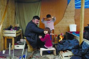 Родина курдів з Іраку гріються поблизу дерев’яного будинку в таборі для мігрантів у Франції