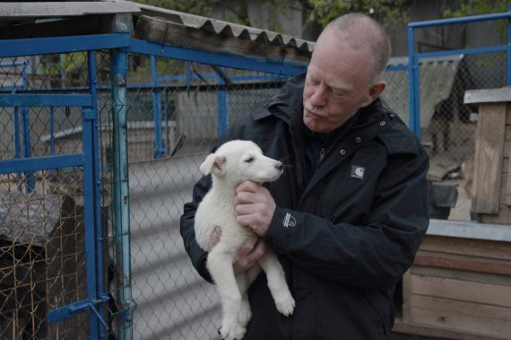 Чоловік тримає на руках цуценя. Власники приносять собак до притулку Товариства захисту тварин ”СОС” або лишають їх під воротами