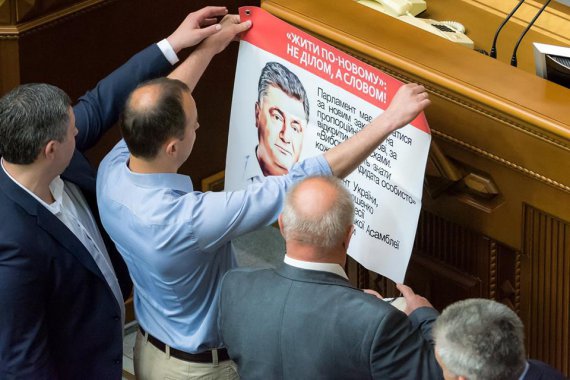 Народные депутаты клеят на трибуну плакат с изображением президента Петра Порошенко и его лозунгом "Жить по-новому"