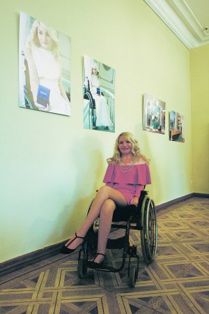 42-річна Олена Котляренко із Чернігова сидить біля своїх фотографій у Національному музеї Тараса Шевченка в столиці. У фотопроекті ”Нескорена краса” має образ закоханої. Пересувається на візку, відколи 23-річною отримала травму шиї