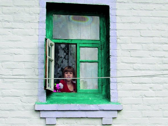 Першокласниця Марія Фень дивиться з вікна свого будинку. Приїхала з батьками до Ціпків із-під Попасної Луганської області