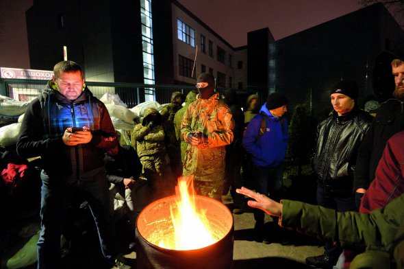 Чоловіки гріються біля бочок із багаттям навпроти будівлі телеканалу NewsOne у Києві. 3 грудня офіс заблокували кілька десятків активістів партії “Братство”. Вимагають, аби власник каналу Євген Мураєв вибачився за те, що назвав Революцію гідності державним переворотом