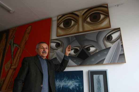 Александр Мельник указывает на собственную картину "Вижу дела твои, человек!". На ней изображены глаза Господа. 20 февраля 2014 в полотно попало три резиновые пули.