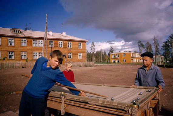 Мальчики в Братске играют в бильярд, сделанный своими руками, и покрытый старым одеялом. Здание на заднем плане – одно из первых в Братске.