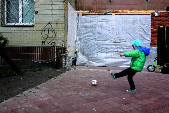 Хлопчик грає у футбол на Оболонській набережній у Києві. Тут на стіні будинку фанати московського ”Динамо” залишили графіті з емблемою свого клубу