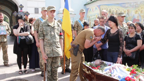 Друг Вячеслава Куцмая целует руку матери на похоронах 26 мая. "Я сидел с ним спина к спине. Все мало прилететь мне, попало в него", - говорит боец