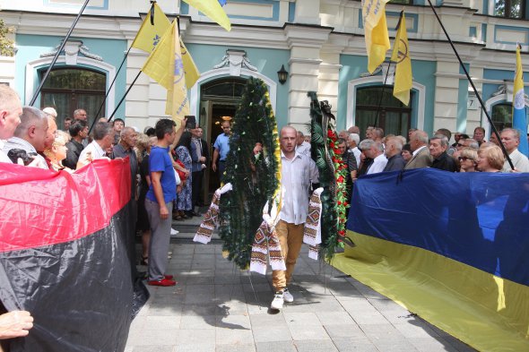 По обидва боки коридору для труни люди тримають синьо-жовтий і червоно-чорний прапори