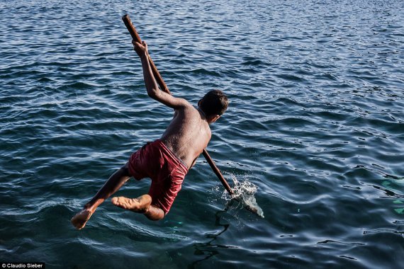 Китобои, среди которых много подростков, прыгают на китов с деревянными копьями