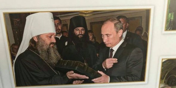 Фотовыставка о возрождении духовной жизни в лавре. Священник Павел связывает это со  своей фотографией, где он с Владимиром Путиным, которую поместили среди других снимков на выставке.