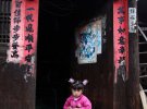 Маленькая девочка сидит у дверей собственного дома в провинции Шеньджоу, Китай