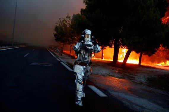 Пожарный надел огнестойкую форму во время лесных пожаров неподалеку греческих Афин. В огне погибли по меньшей мере 88 человек. Возгорание, предположительно, началось из-за халатности - незатушенного костра. 23 июля