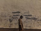 "Мальчик с Алмаджири". Здесь изображен ребенок в городе Бол в Чаде под стеной, разрисованной изображениями гранатометов. Из-за значительного высыхания озера Чад - некогда крупнейшего в Африке - на его берегах царит голод и постоянные конфликты фермеров и скотоводов. В этом районе активной является группировка "Боко Харам", которая пополняет здесь ряды своих бойцов.