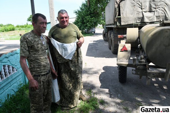 Волонтери передають військовим плащ-палатки і солодощі. Бійця справа звуть Василь. Разом із ним служить син