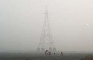 Люди йдуть біля опори лінії електро­передачі в індійській столиці Делі. Влада просить не виходити на вулицю з маленькими дітьми, тих, у кого є захворювання серця чи легень. Лікарні переповнені