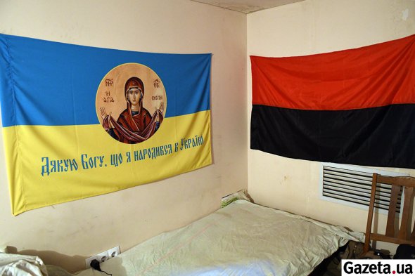 Сине-желтый и красно-черные флаги над кроватью в комнате старшего сержанта Виталия. Живет в в подвале под Авдеевским отделом полиции пока ищет жилье