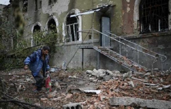 Местный житель Донбасса с пакетом в руках роется в поисках уцелевших вещей. Здание позади него разбита от российских обстрелов по мирным жителям