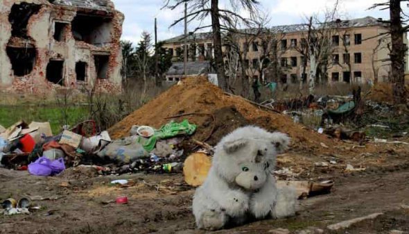 Мягкая детская игрушка - уже серый мишка на фоне здания разрушенной от артиллерийского обстрела, который совершили русские захватчики на Донбассе