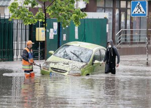 Двоє чоловіків роздивляються частково затоплений автомобіль на вулиці Києва 4 травня. Містом пройшла злива, в деяких районах випав град. Вода залила дороги й підземні переходи. Подібні дощі можливі в столиці до кінця тижня, кажуть синоптики