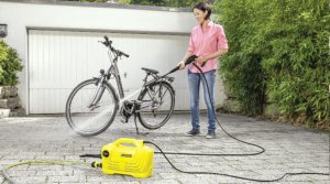 Жінка миє велосипед за допомогою електричної мийки. Пристрій подає воду під тиском 160 барів. Струмінь швидко очистить фасад будинку, машину, тротуарну плитку