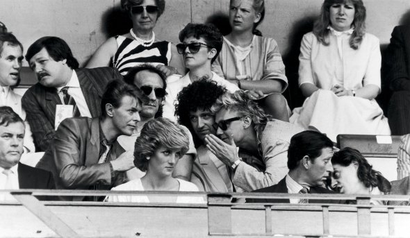 Організатор благодійного концерту Live Aid Боб Ґелдоф (крайній праворуч у першому ряду) спілкується з принцом Вельським Чарльзом на трибуні Wembley Stadium, 13 липня 1985 року. Біля них – принцеса Діана. Позаду розмовляють співак Девід Бові та музиканти гурту Queen Роджер Тейлор і Браян Мей