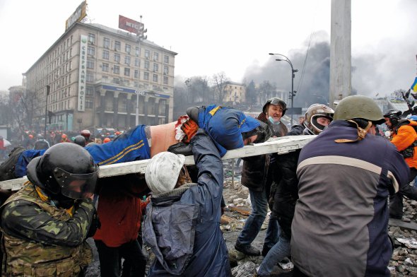 Протестувальники тримають на ношах пораненого чоловіка. Люди вийшли на Майдан на підтримку європейського вектора зовнішньої політики України. Акції почалися 21 листопада 2013-го після рішення влади не підписувати Угоди про асоціацію з Євросоюзом. Коли ”беркутівці” побили студентів, протести переросли у виступи проти корупції і свавілля правоохоронних органів – Революцію гідності. Силовики застосували зброю. Загинули 107 мітингарів. Їх назвали Небесною сотнею. Київ, майдан Незалежності, 20 лютого 2014 року