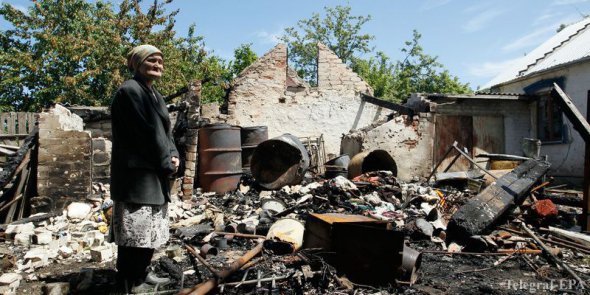 Пожилая женщина осматривает руины. Пожарище - это все, что осталось от ее дома после российского обстрела.