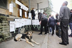 Люди стоять у черзі до дільниці у селищі Коцюбинське під Києвом 25 жовтня. Читають розвішані на сходах і поручнях списки кандидатів