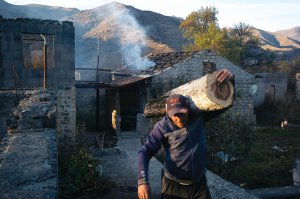 Чоловік несе колоду в місті Кельбаджар. Позаду горить його будинок. Вірменія до 26 листопада має передати Кельбаджарський район Азербайджану. Тікаючи з Нагірного Карабаху, вірмени спалюють те, що не можуть взяти з собою. Дерева пиляють на дрова. Вантажівок із деревиною на трасі чи не більше, ніж машин із речами